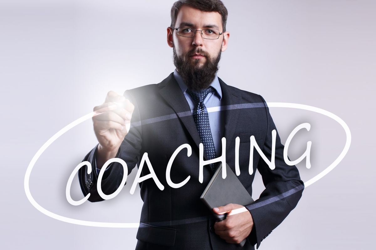 Businessman writing "Coaching" with marker on transparent board.